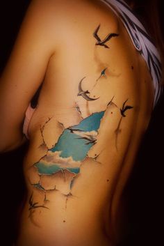 a woman's back with birds flying in the sky on her side and behind her