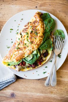 an omelet with spinach and other vegetables on a plate next to a fork