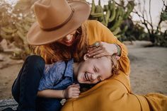 a woman in a yellow jacket and hat hugging a young boy who is wearing a cowboy hat