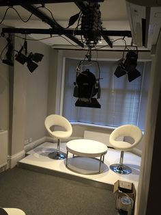 an empty room with two chairs and a table in the corner, lighting equipment hanging from the ceiling