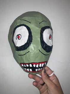 a hand holding up a paper mache with eyes and mouth