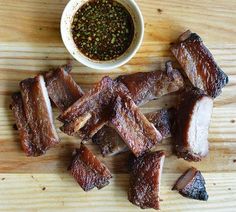 some ribs are on a wooden table next to a small bowl of seasoning sprinkles