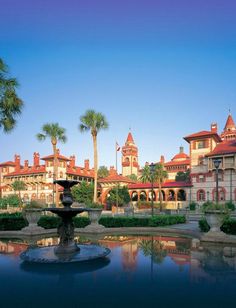 a fountain in front of a large building with palm trees on the other side and water feature