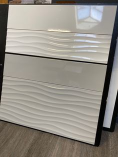 a white and black dresser sitting on top of a wooden floor next to a wall