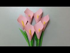 three pink flowers with green stems on a gray surface and one is cut out from paper