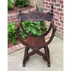 a wooden chair sitting on top of a sidewalk next to a planter filled with green plants