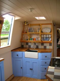 a kitchen with blue cabinets and white dishes on the counter top, in front of a window