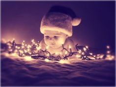 a baby wearing a santa hat laying on top of a bed covered in christmas lights