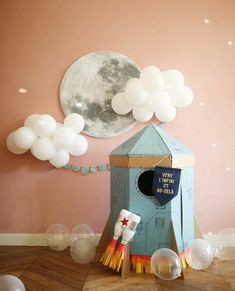 a room decorated with balloons and a blue birdhouse shaped like a rocket ship in front of the moon