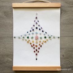 a cross stitch pattern on a white piece of cloth with beads and pins attached to it