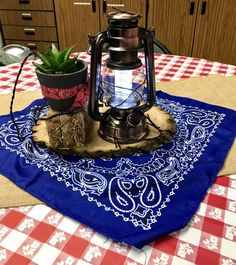 a table with a red and white checkered table cloth, an old fashioned kerosen lamp on it