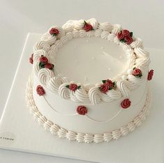 a white cake with red roses on it sitting on top of a table next to a napkin