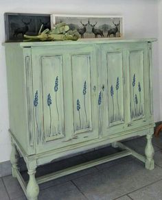 an old green cabinet with blue flowers painted on the doors and drawers, in front of a white wall