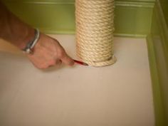 a person is using a brush to paint a piece of rope on the floor next to a roll of twine