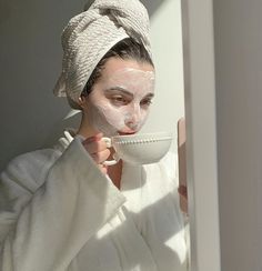 a woman with a towel on her head is holding a cup in front of her face