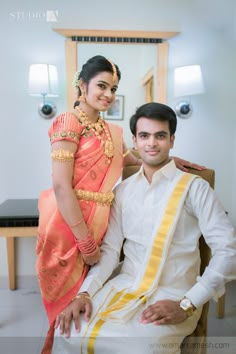 a man sitting next to a woman in a white and orange dress on a chair