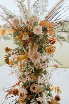 a tall vase filled with lots of flowers and greenery on top of a table