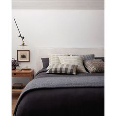 a bed with black and white pillows on it next to a night stand, lamp and nightstand