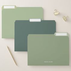 three green folders sitting on top of a table next to a pen and pencil