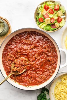 a large pot filled with spaghetti next to bowls of pasta and salad on the table