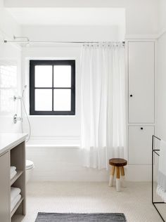 a white bathroom with a black window and rug on the floor in front of it