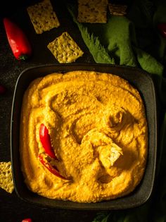 a square pan filled with yellow hummus and tortilla chips on the side