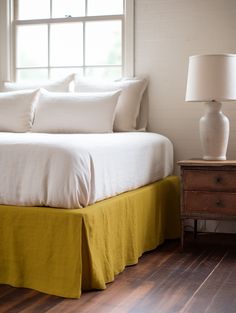 a bed with white sheets and yellow bedspread in front of a large window