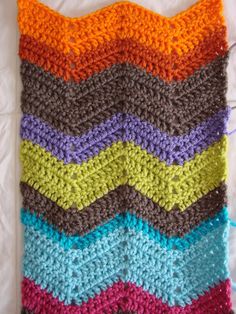 a multicolored crocheted blanket is laying on a white sheet with yarn