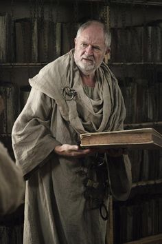 an old man holding a book in front of a bookshelf full of books