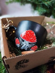 a painted egg in a cardboard box on the ground next to christmas ornaments and decorations