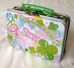 a green and pink tin case sitting on top of a bed next to a white sheet