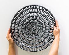 two hands holding a decorative plate on top of a white tableclothed surface with an intricate design