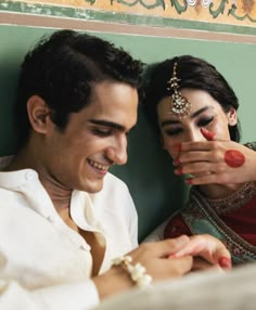 a man and woman sitting next to each other with makeup on their faces while looking at the camera