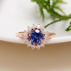 a blue and white diamond ring sitting on top of a plate next to a plant