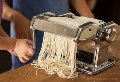 a person is using a pasta maker to make spaghetti on a wooden table with other people in the background