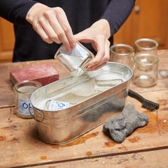 a person pouring water into a metal container on top of a wooden table next to other items