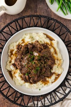 a white bowl filled with mashed potatoes and beef on top of a wooden table