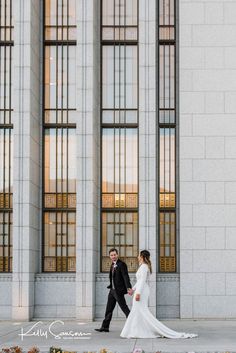 a bride and groom walking together in front of an old building with tall glass windows