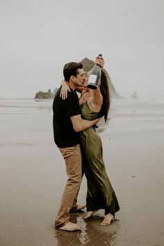 a man and woman kissing on the beach while holding an empty bottle in front of them