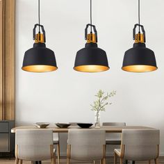 three black and gold pendant lights hanging from the ceiling above a dining room table with beige chairs