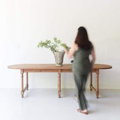 a woman walking past a table with a potted plant on it