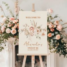 an easel with a welcome sign on it in front of some pink and white flowers