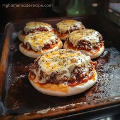 four mini pizzas sitting on top of a baking pan covered in cheese and sauce