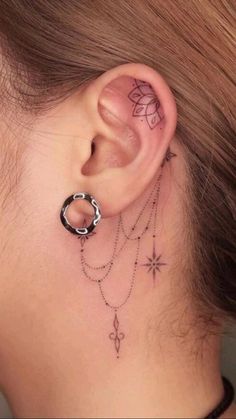 a woman's ear with tattoos on it and a chain hanging from the side