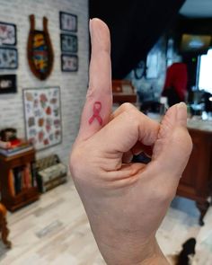 a person's hand with a pink ribbon on the middle finger in front of a desk