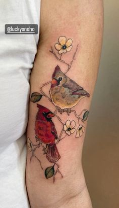 a woman's arm with two birds sitting on top of flowers and leaves in the background