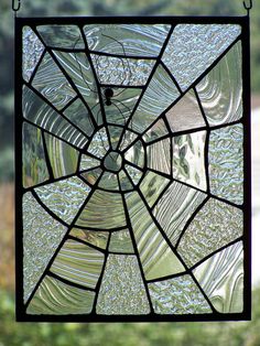 a stained glass window hanging in front of a green grass covered hillside with trees behind it