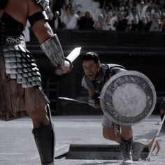 two men dressed in roman armor, one holding a shield and the other kneeling down