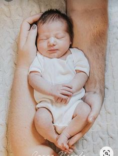 a man holding a baby in his arms while laying on top of a white blanket