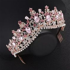 a tiara with pink and white stones on it sitting on a black surface in front of a black background